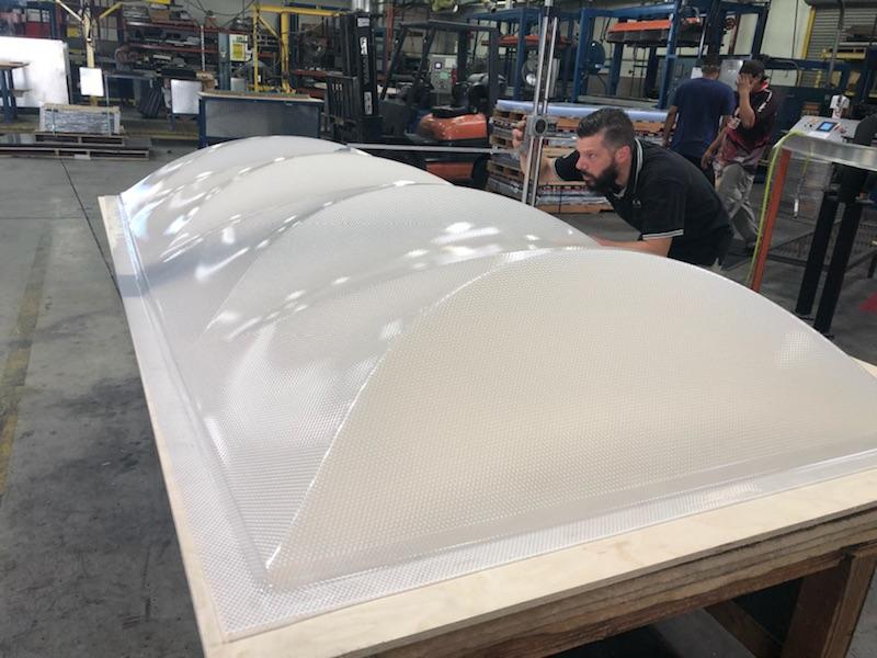 A man inspects a large, translucent, dome-shaped panel in a factory setting.